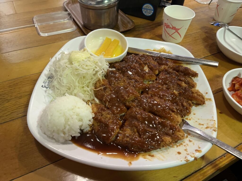 A large Korean donkatsu covered in brown sauce, served with rice, shredded cabbage, and pickled radish at Donzanchi in Seoul