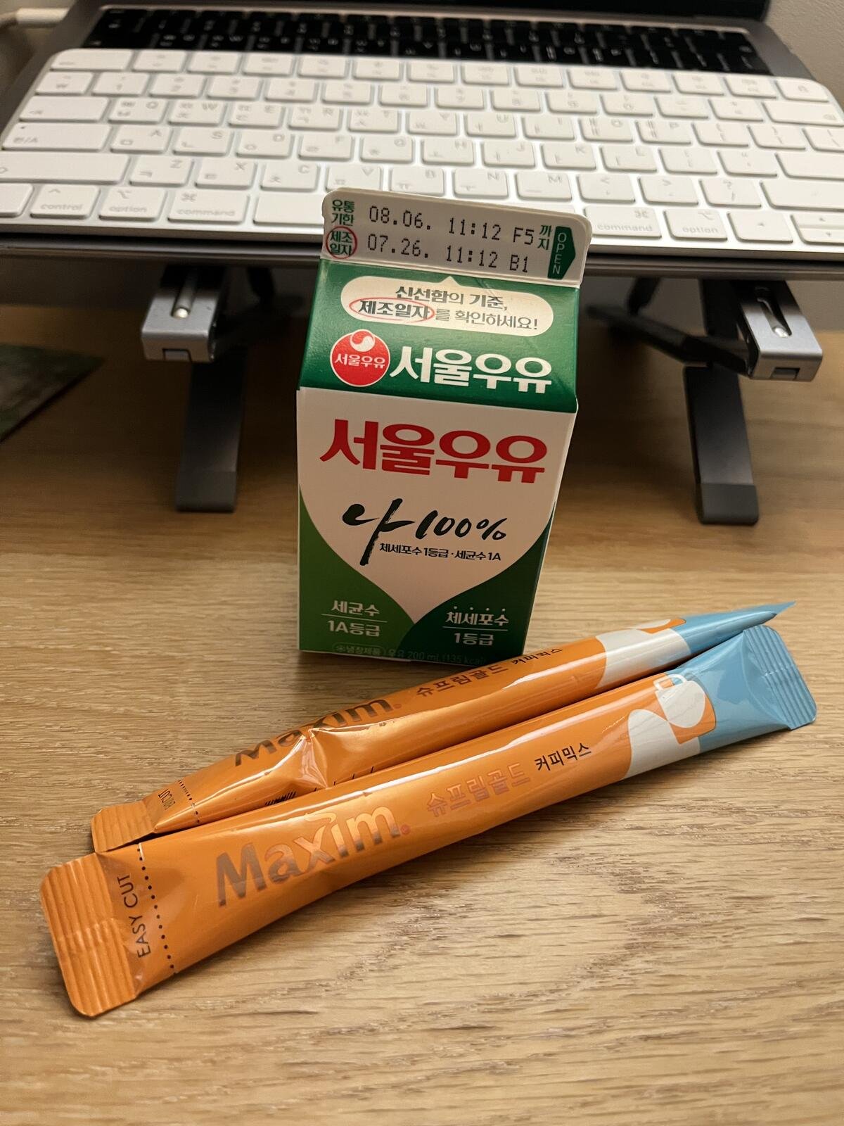A 200ml carton of Seoul Milk next to two Maxim Supreme Gold Korean coffee mix sticks on a desk.