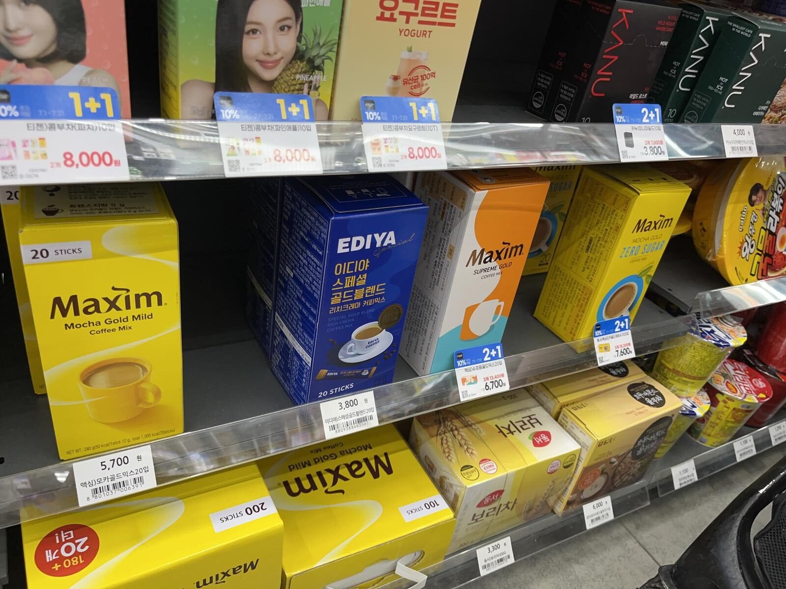 A Korean supermarket shelf stacked with boxes of Maxim Korean coffee mix in several sizes.