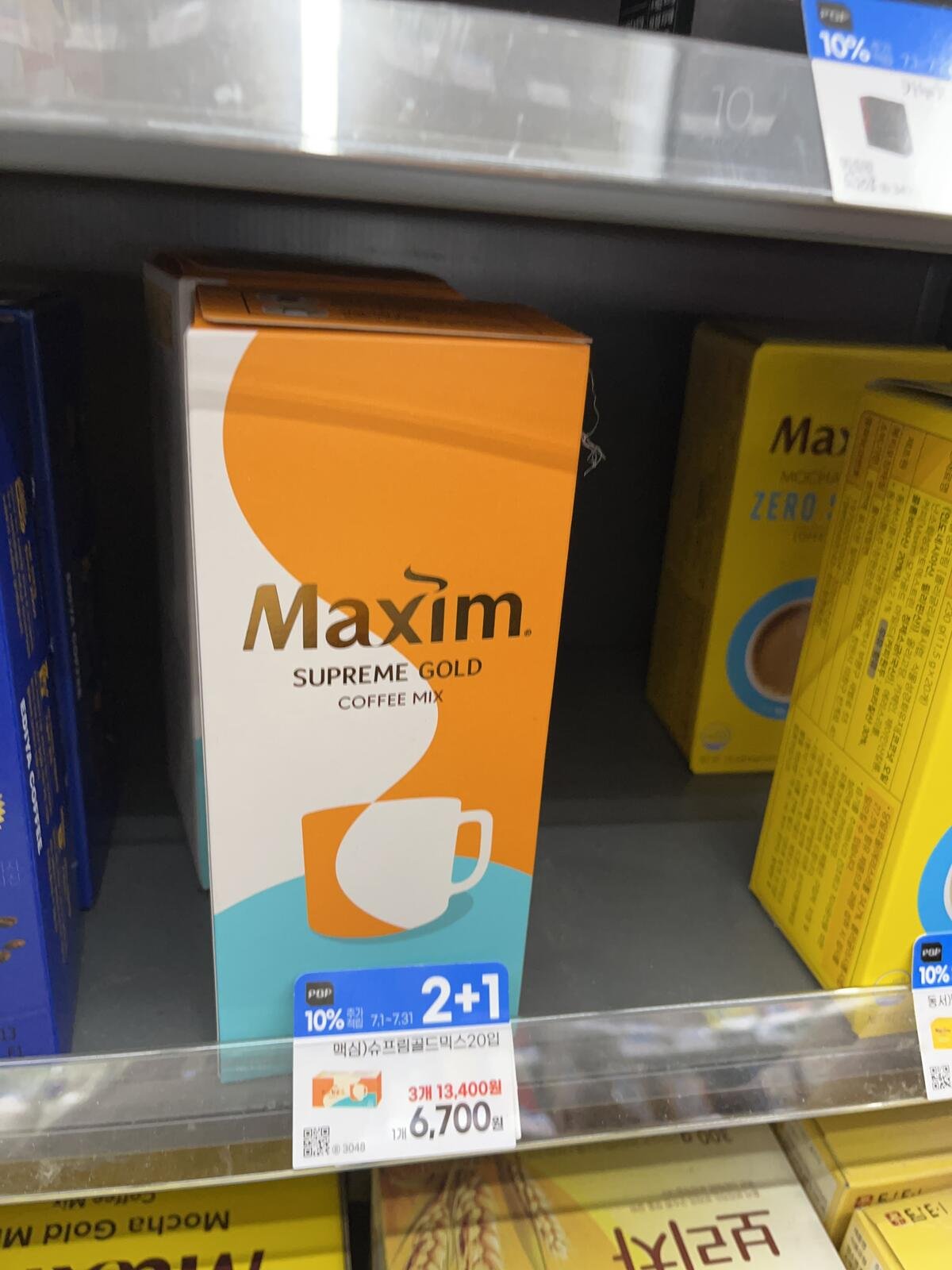 A box of Maxim Supreme Gold Korean coffee mix on a supermarket shelf with its price tag.