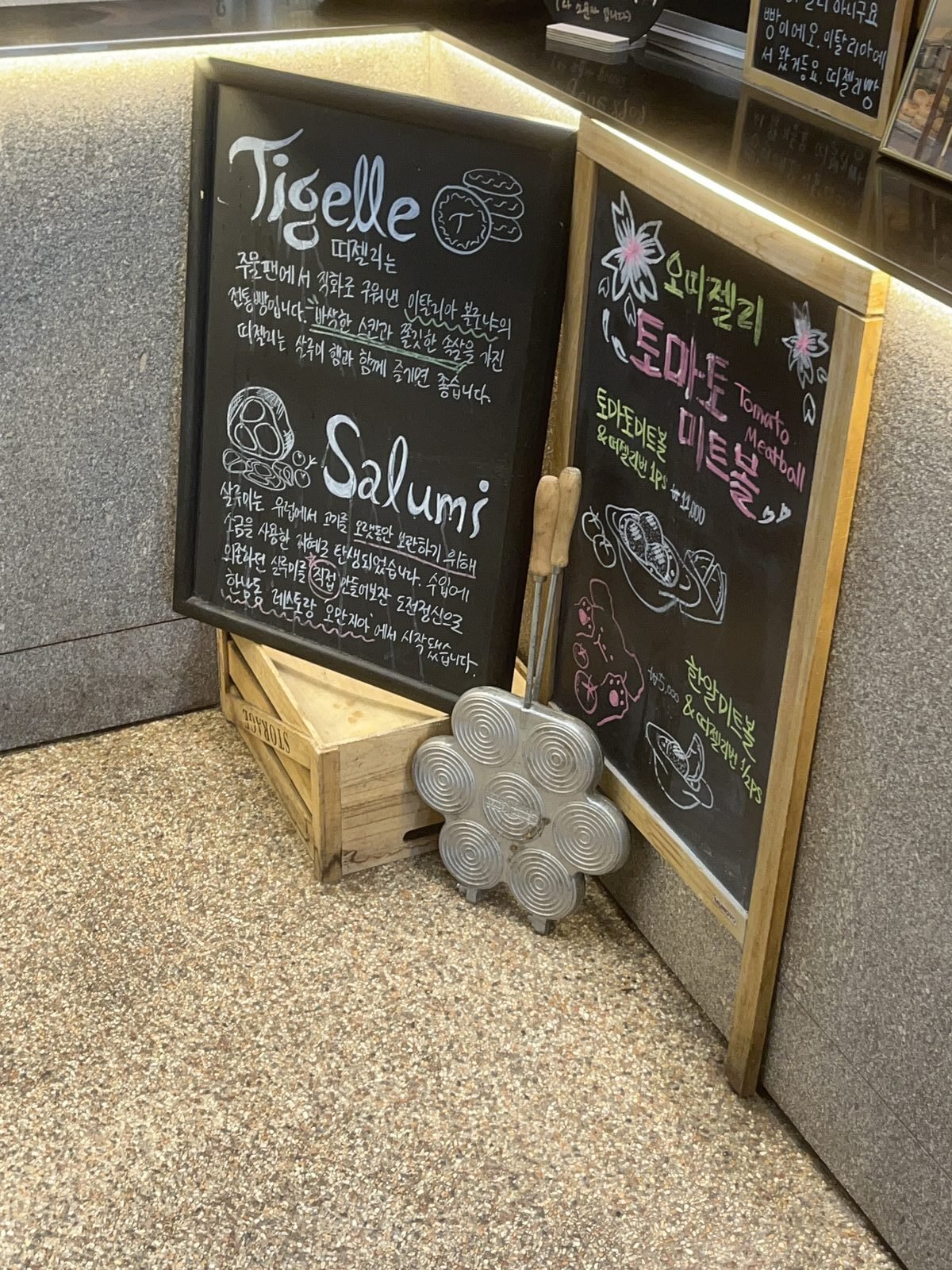 Chalkboards explaining tigelle and salumi at O Tigelle, with the metal tigelliera pan propped beside them