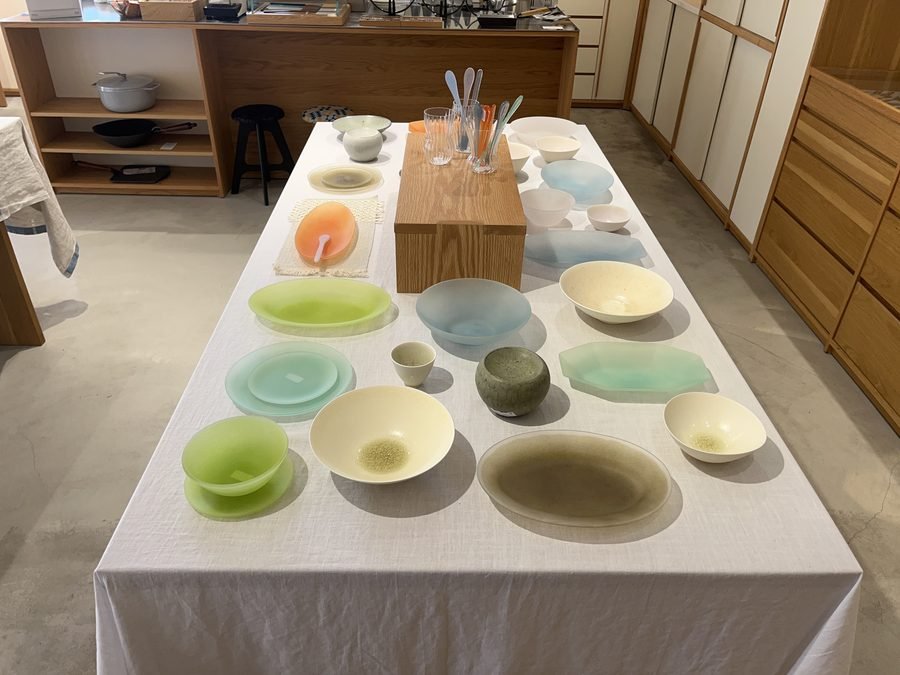 Pale green and cream ceramic plates and bowls laid out on a long table on the second floor.