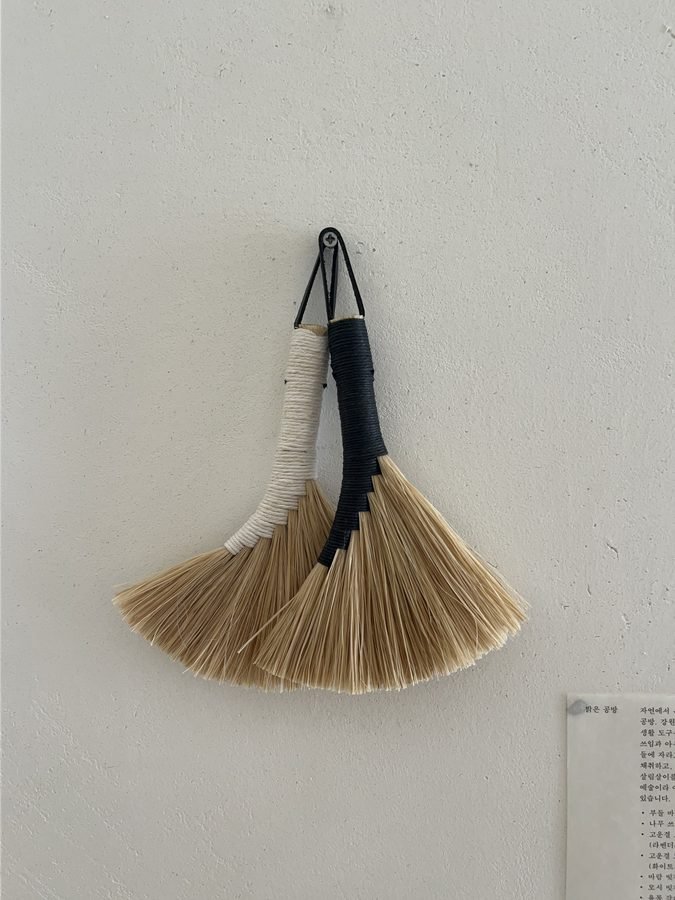 A tea whisk hanging on a white wall next to a card describing it.