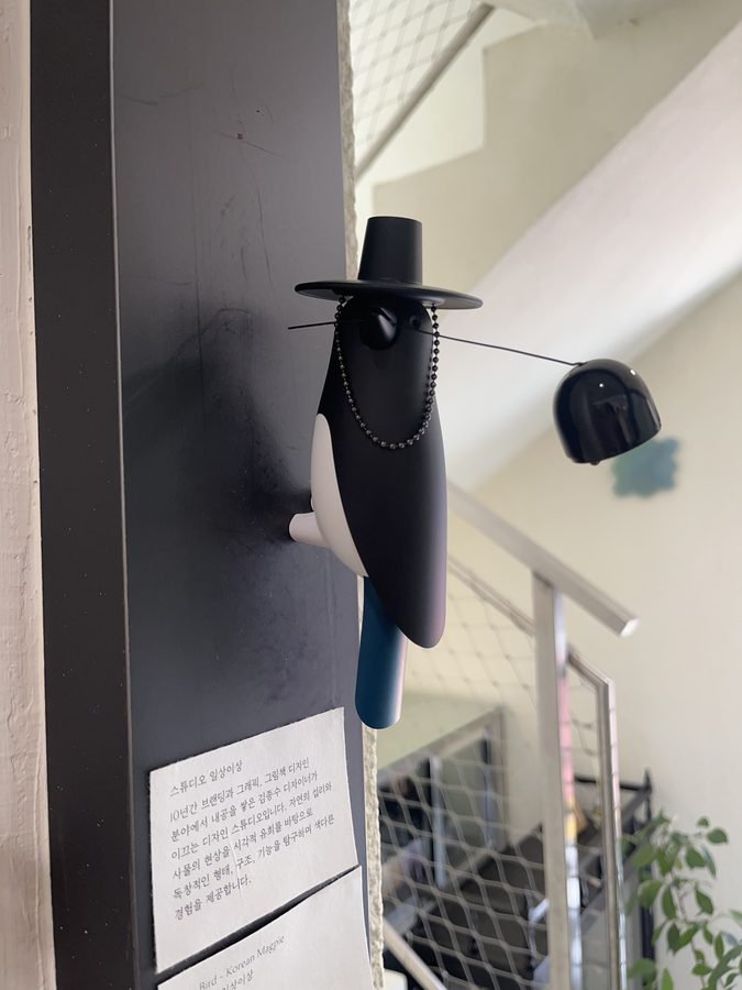 A hanging bird figure in a wide-brimmed hat on a dark wall.