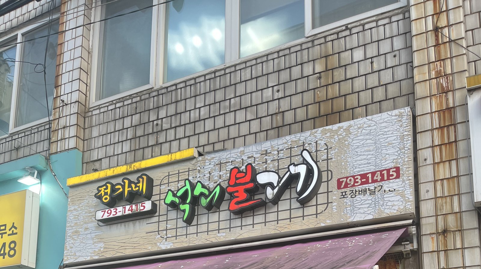 The green sign above the door reading Jeonggane Seokswoe Bulgogi, cracked and lifted in patches.