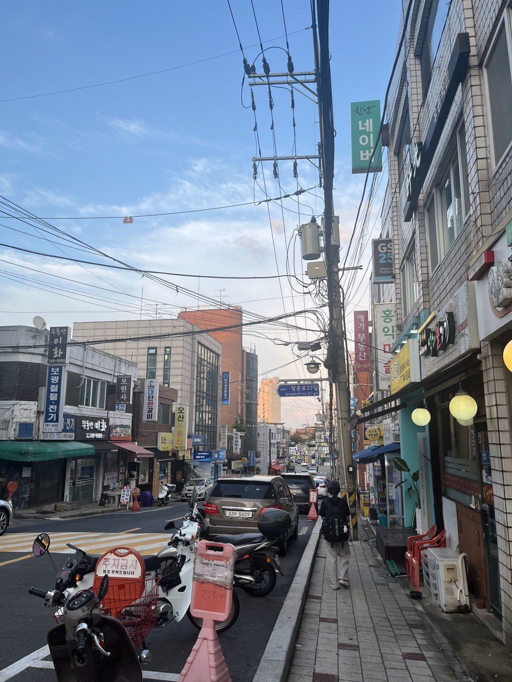 The street outside in Bogwang-dong: low buildings, overhead wires, parked motorbikes.